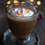 A sugar-free Keto Peppermint Mocha in a glass mug on a dark wooden table, with christmas lights in the background.