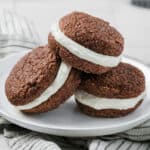 Three Keto Gingerbread Whoopie Pies piled up on a white plate over a striped napkin.