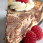 Titled image of a slice of keto marble cheesecake on a white plate with raspberries.
