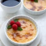Two fluted white ramekins filled with keto creme brûlée with fresh raspberries and mint leaves on top.