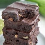 A stack of brownies with chocolate frosting on a white plate, with a bite taken out of one. Title at the top says The Best Keto Recipes of 2025.