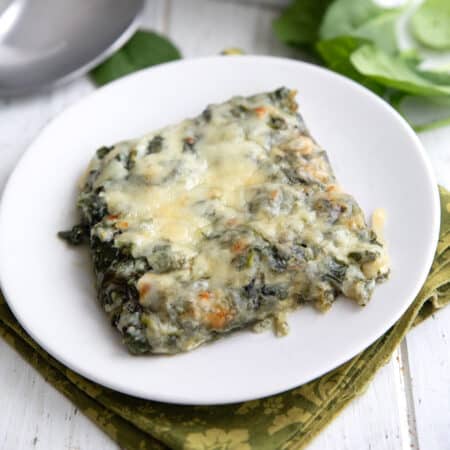 A serving of Cheesy Spinach Casserole on a white plate over a green patterned napkin.