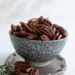 Salted pecans piled up in a flecked gray bowl on a marble table top.