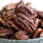 Close up shot of salted pecans with rosemary in a flecked gray bowl.