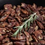 Titled image for Rosemary Salted Pecans in a black iron skillet with a sprig of rosemary on top.