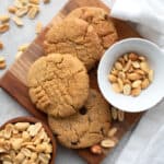 Top down image of Keto Air Fryer Peanut Butter Cookies on a small wooden cutting board with peanuts strewn around.