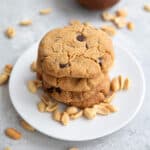 A stack of Keto Air Fryer Peanut Butter Cookies on a white plate with peanuts strewn around.