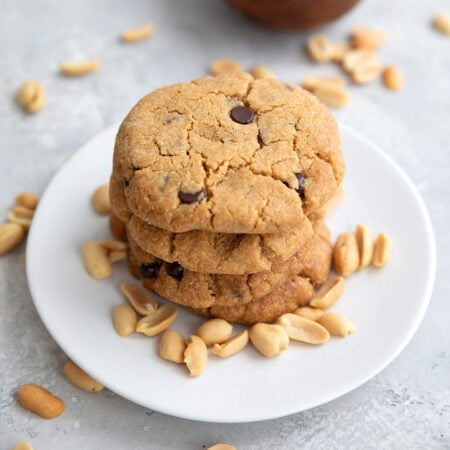 A stack of Keto Air Fryer Peanut Butter Cookies on a white plate with peanuts strewn around.