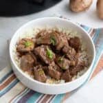 Slow Cooker Beef Tips in a white bowl over a striped napkin.