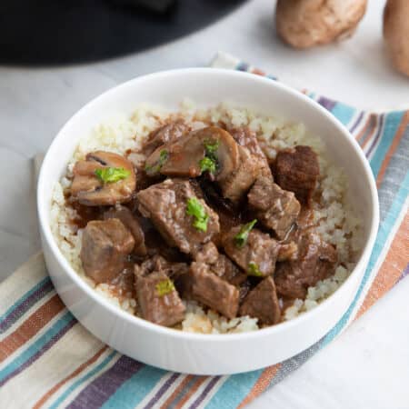 Slow Cooker Beef Tips in a white bowl over a striped napkin.