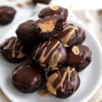Keto Buckeye Bites piled up on a white plate with one cut in half to show th inside.