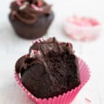 keto chocolate cupcake with chocolate frosting with a bite taken out of it in a pink cupcake liner on a white table.