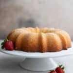 Keto Kentucky Butter Cake on a white cake stand with a strawberry. The cake is a large golden fluted bundt cake.