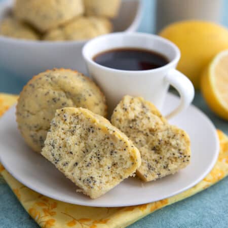 Lemon Poppyseed Protein Muffins on a white plate with a cup of coffee, over a yellow flowered napkin.