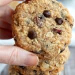 Titled image of a hand holding up a Keto Oatmeal Cookie above a stack of more cookies.