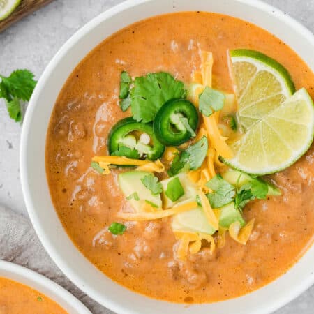 Top down image of Keto Taco Soup in a white bowl with cheese, avocado, and jalapeños on top.