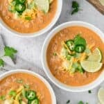 Top down image of three white bowls filled with Keto Taco Soup, with cheese, avocado, and jalapeños on top.