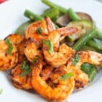 Chili Garlic Shrimp on a white plate with sautéed vegetables, with chopped parsley on top.