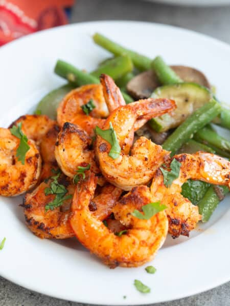 Chili Garlic Shrimp on a white plate with sautéed vegetables, with chopped parsley on top.