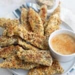 Keto chicken tenders with everything bagel seasoning piled up on a white plate over a blue and white striped napkin.