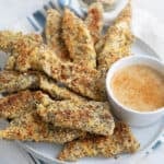 Keto chicken tenders with everything bagel seasoning piled up on a white plate over a blue and white striped napkin.