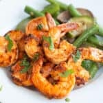 Chili Garlic Shrimp on a white plate with sautéed vegetables, with chopped parsley on top.