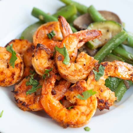 Chili Garlic Shrimp on a white plate with sautéed vegetables, with chopped parsley on top.