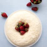 Top down image of a keto coconut bundt cake on a white plate with strawberries piled up in the center.