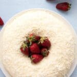 Titled image top down of a keto coconut cake with strawberries on a blue table top.