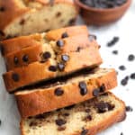 Keto Chocolate Chip Loaf Cake in slices on a piece of white parchment paper, with chocolate chips strewn around.