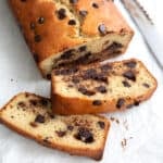 Two slices of Keto Chocolate Chip Loaf Cake on white parchment paper in front of the loaf.