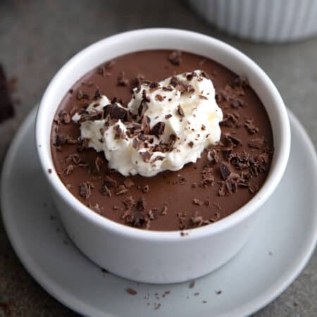 Close up shot of Keto Blender Chocolate Mousse in a white bowl on a small gray plate, with whipped cream on top.