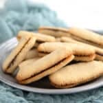 Keto Milano Cookies piled up on a pewter plate over a gauzy teal napkin.