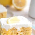 Titled image close up of Keto Lemon Poke Cake on a white plate with a forkful taken out of it.