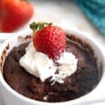 Titled image of a keto chocolate protein mug cake in a white ramekin with whipped cream and strawberries on top.