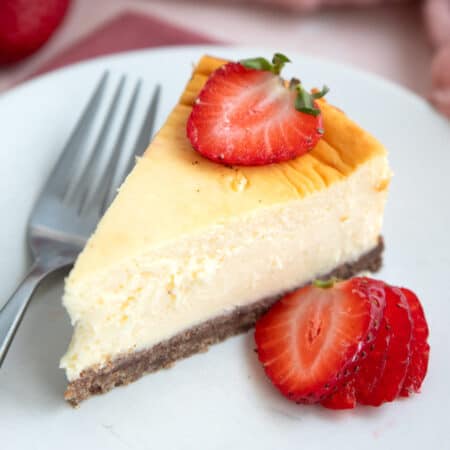 A slice of Keto Air Fryer Cheesecake on a white plate with sliced strawberries.