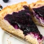 Titled image of a slice of Keto Blueberry Coffee Cake being pulled away from the rest of the cake.