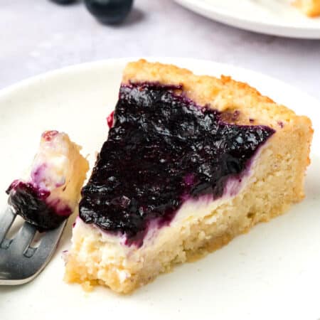 A slice of Keto Blueberry Cream Cheese Coffee Cake on a white plate with a forkful taken out of it.