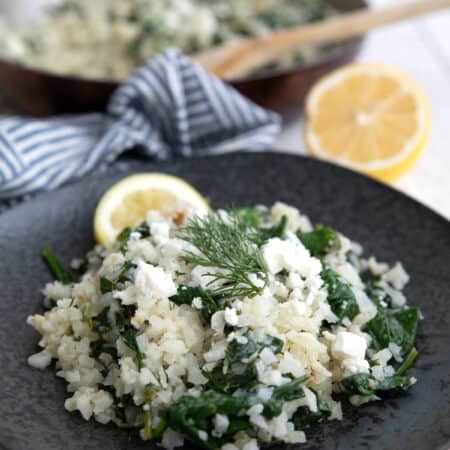 Close up shot of Keto Greek Cauliflower Rice on a black plate with a slice of lemon.