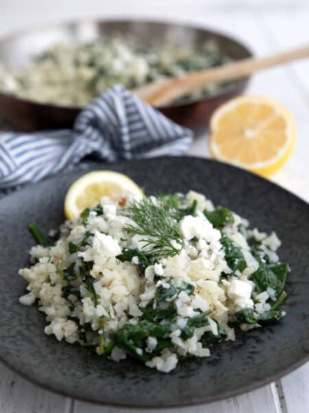 Close up shot of Keto Greek Cauliflower Rice on a black plate with a slice of lemon.