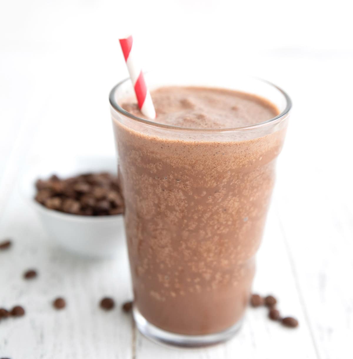 A keto coffee protein shake on a white table top with a striped red straw.