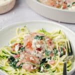 A serving of Spinach Feta Chicken sits atop zucchini noodles on a white plate with a fork.