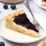 A slice of Keto Blueberry Coffee Cake on a white plate with a fork.