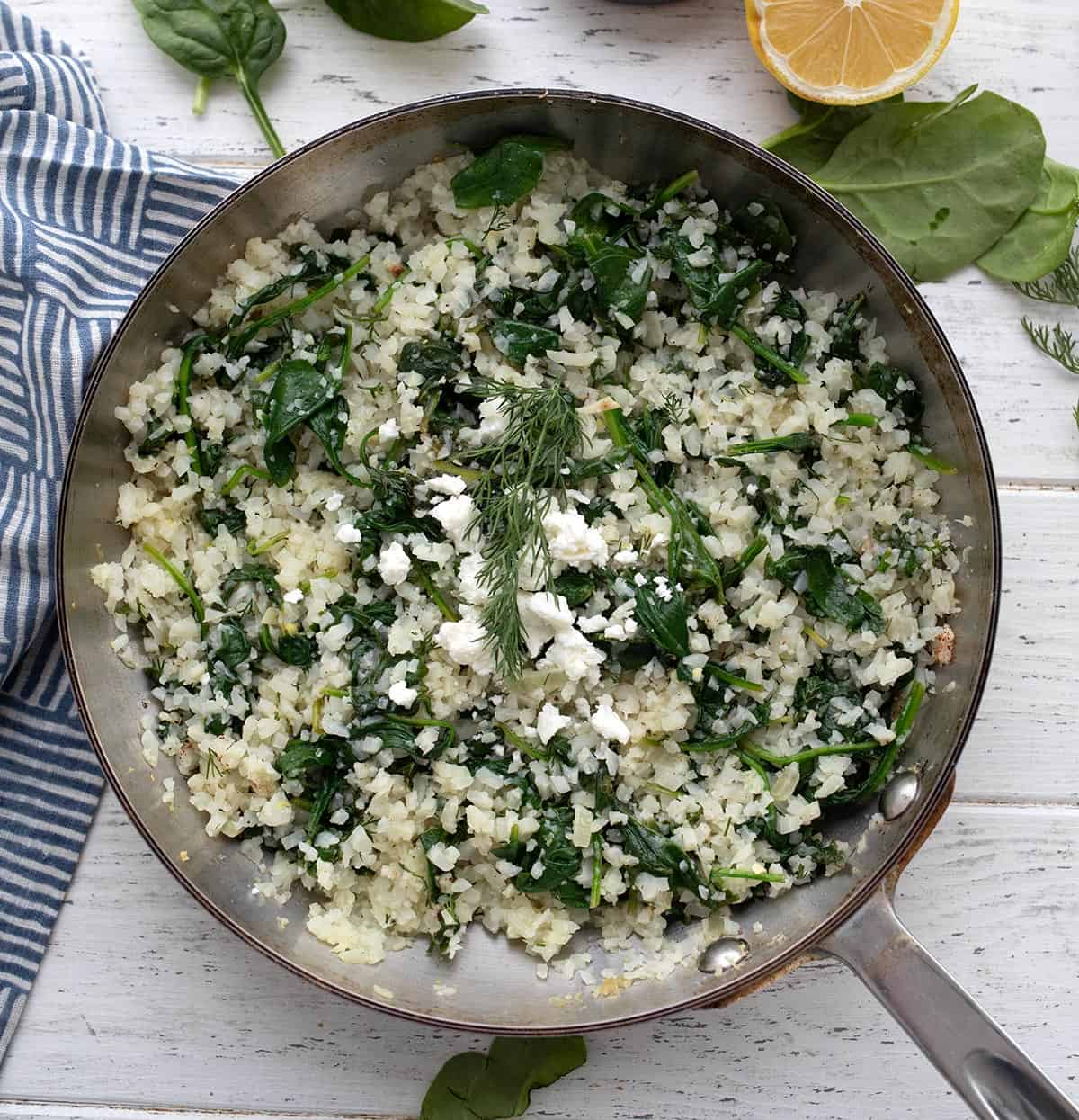 Top down image of Keto Spanakorizo in a stainless steel skillet on a white wooden table.