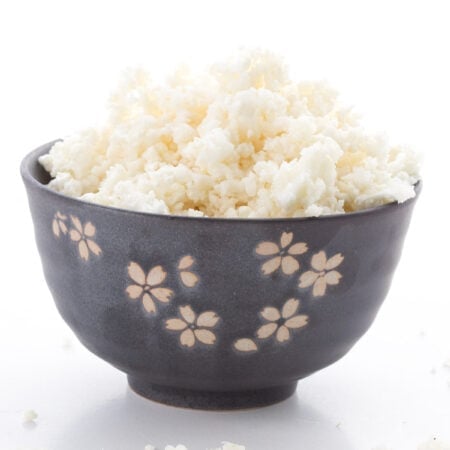 A black bowl with engraved flowers filled with cauliflower rice on a white background.