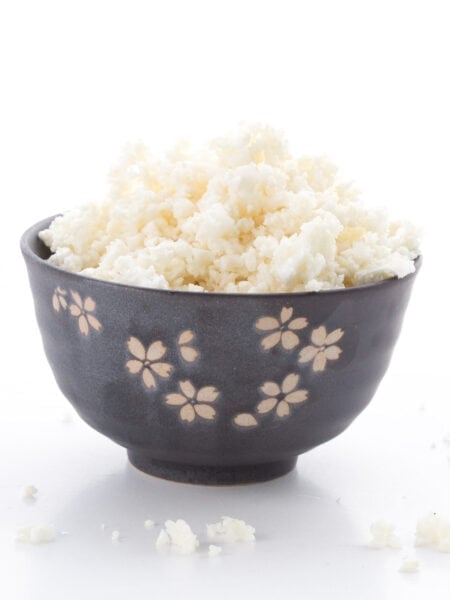 A black bowl with engraved flowers filled with cauliflower rice on a white background.