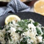Titled image of keto spinach cauliflower rice on a black plate with a slice of lemon.