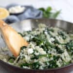 A wooden spoon digging into a pan of Keto Spanakorizo (Greek Cauliflower Rice with Spinach).
