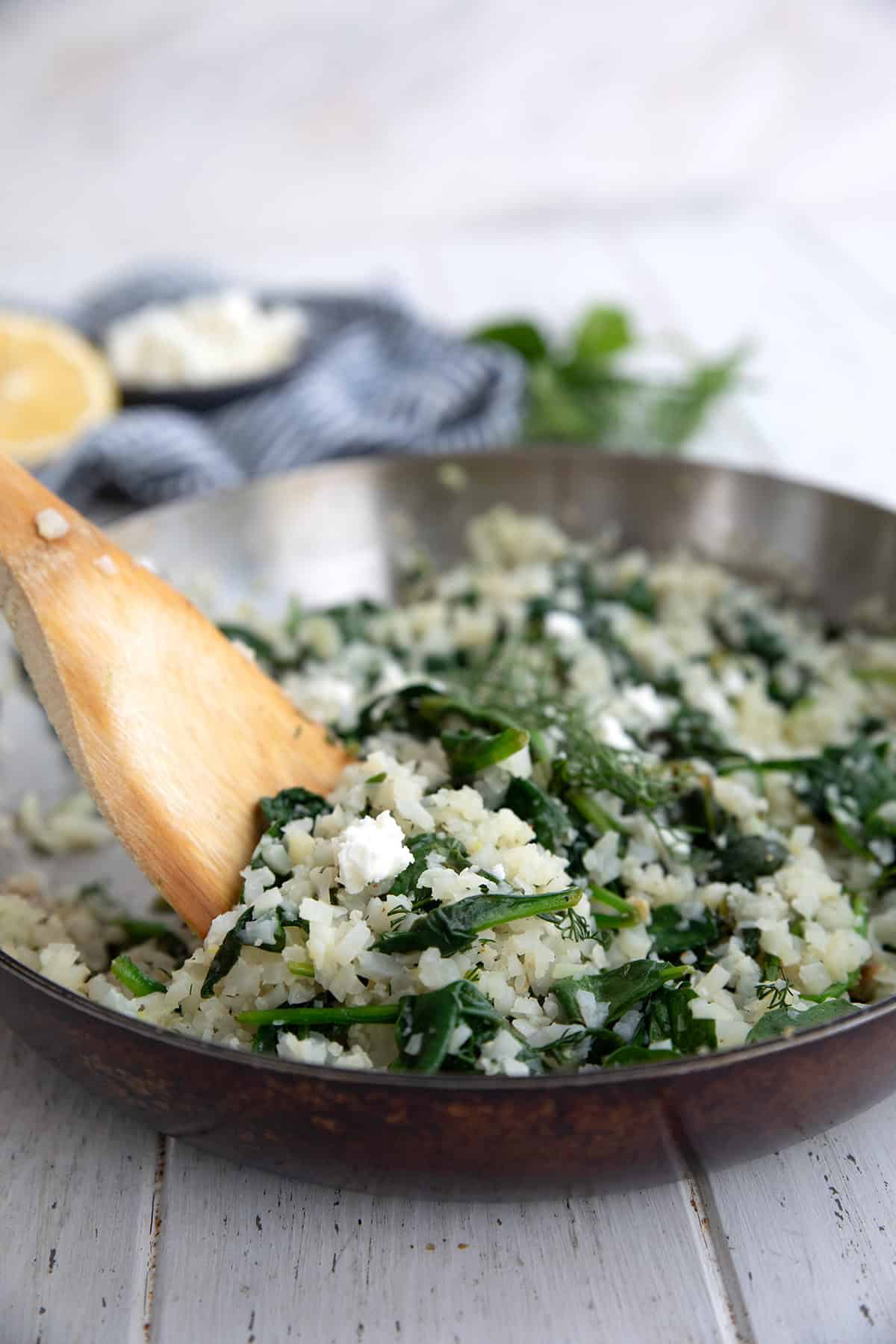 A wooden spoon digging into a pan of Keto Spanakorizo (Greek Cauliflower Rice with Spinach).