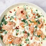 Titled image of a white enameled skillet filled with creamy spinach feta chicken.